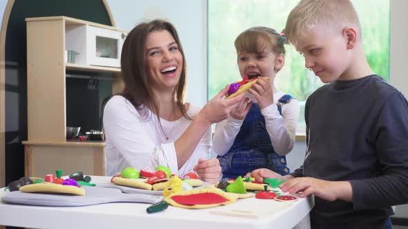 Caucasian girl and boy kid playing and learning at preschool with female teacher. Mother, daughter a