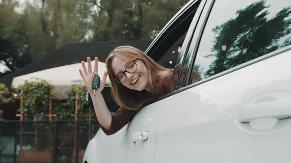Happy Face Expression of Young Caucasian Woman Sitting on the Driver Seat and Waving with Car Keys