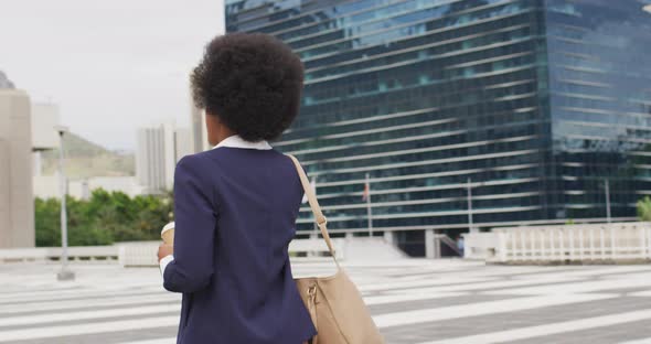 African american businesswoman holding takeaway coffee and talking on smartphone