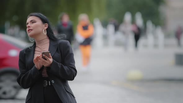 Closeup Businesswoman Stands Outdoors in City Near Roadway Holding Mobile Phone Looking Around