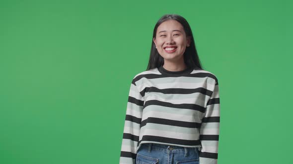 A Smiling Asian Woman Dabbing While Standing In Front Of Green Screen Background
