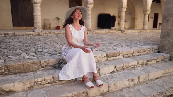 Wide Shot Happy Beautiful Woman in White Dress and Straw Hat Sitting on Stairs in Ancient Cyprus
