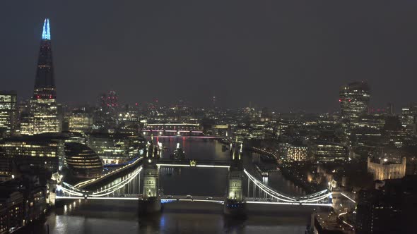 Slow dolly back drone shot of lit up Tower Bridge London thames river at night