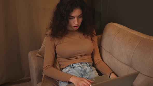 Young Tired Woman Sitting on Couch Yawning While Using Laptop Looking at Screen Lady Browsing