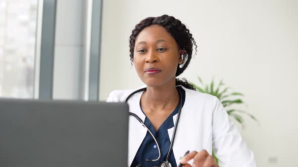 Young African American Woman Doctor with Headset Having Chat or Consultation on Laptop