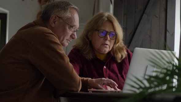 two elderly people surfing internet on laptop computer at home.