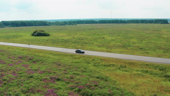 Aerial View of a Driving Car on the Road in a Field Among Lilac Flowers