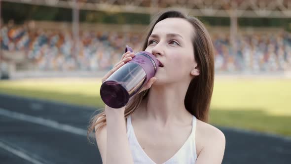 Attractive Sporty Girl in Sportswear Happily Drinking Water After Workout on City Stadium