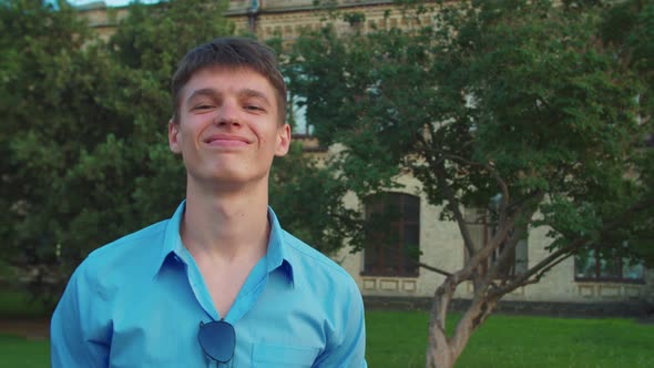 Portrait of Young Man with Forced Smile and Derisive Look Outdoors