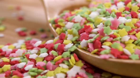 Colorful star cake sprinkles fall in a pile in a wooden spoon on a board