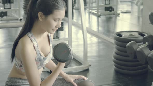 Asian woman bodyweight with lifting dumbbell at fitness.