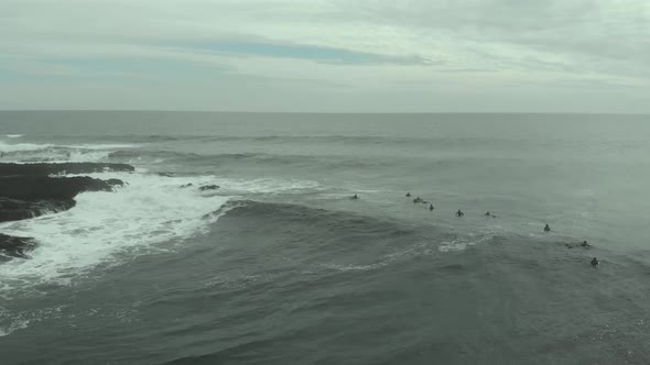 Aerial orbit and reveal of rocky formations and surfers waiting for a wave in Pichilemu, Chile-4K