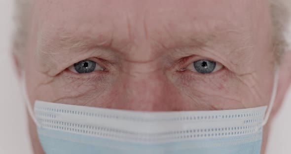 Macro Portrait of Wrinkled Senior Man with Mask Blinks Into the Camera