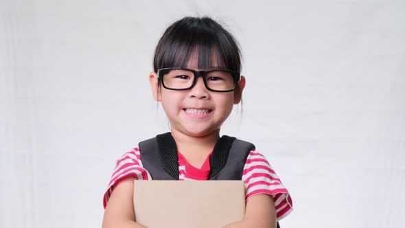 Smiling schoolgirl wearing summer outfit with backpack holding books on white background in