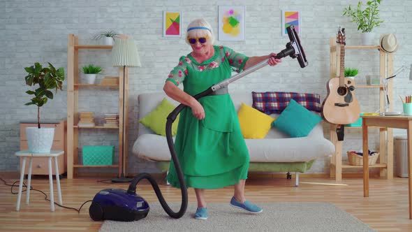 Cheerful Happy Old Woman Pensioner with Gray Hair in Glasses Playing a Vacuum Cleaner Like a Guitar