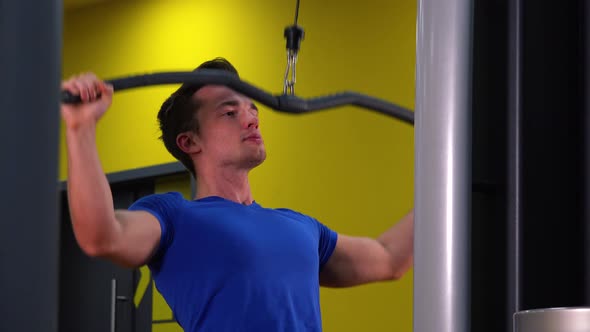 A Young Fit Man Trains on a Cable Tower in a Gym