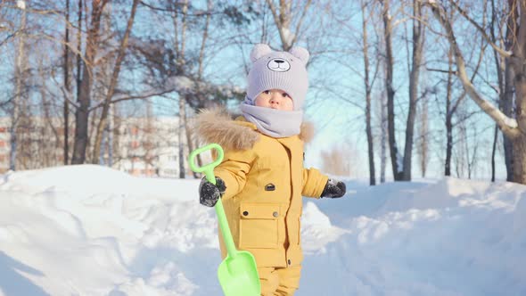 A baby of 15-23 months on a walk in a winter park walks along a snow-covered path. Toddler waves to