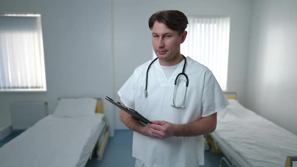 Medium Shot of Intelligent Positive Caucasian Male Doctor Standing in Hospital Ward with Medical