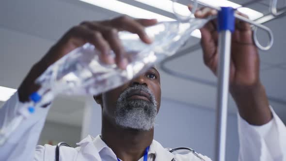 African american male doctor preparing drip bag for patient in hospital room