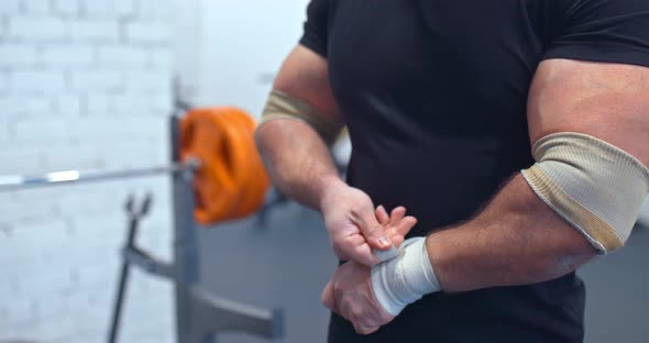 Heavyweight Man Wraps His Wrists with Elastic Bandages Preparing for Sports