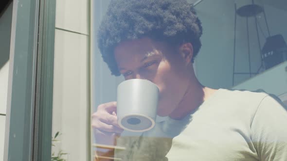 African american man looking at the window and drinking coffee at home