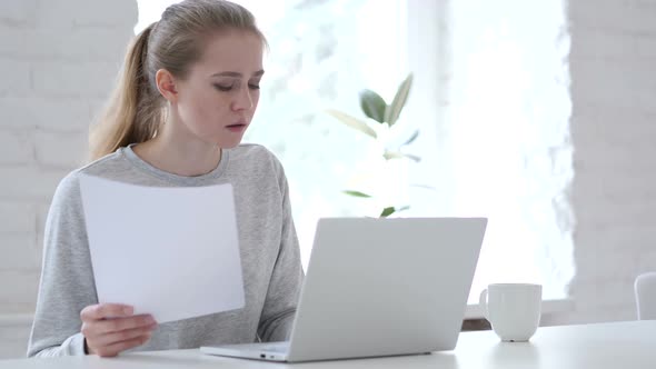 Young Woman Reading Documents and Working on Laptop