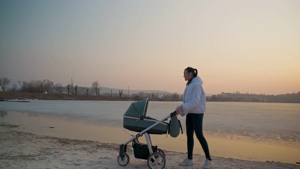 A Young Woman with a Stroller and a Newborn Baby Walking on a Spring Lake