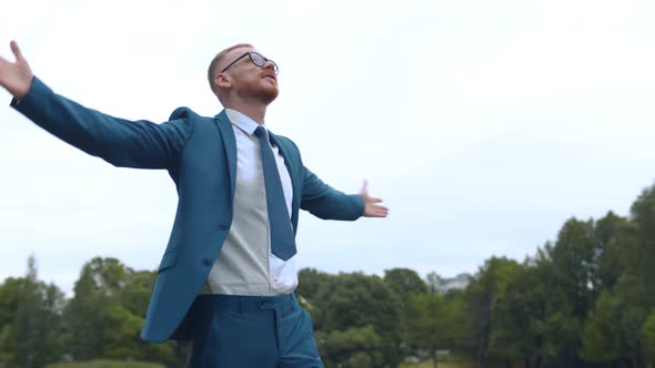 Young Successful Businessman Standing with Arms Wide Open in Summer Park