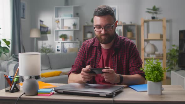 Happy Man is Playing Video Game at Home Using Modern Smartphone