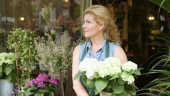 A Florist stands in the doorway of her shop proudly holding a large pot of flowers