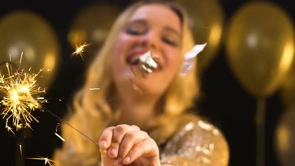 Pretty Blond Female Waving Bengal Light Under Falling Confetti on Party, Prom