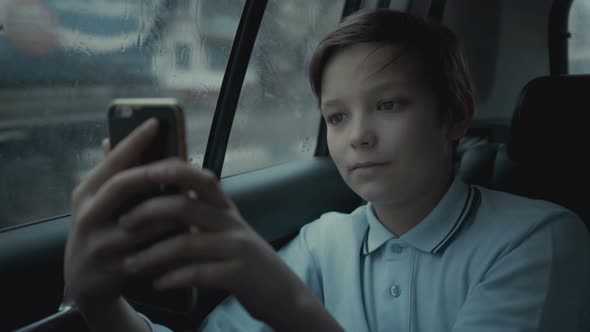 Sad, Unhappy Young Boy Riding in Car Through City During Rainy Day