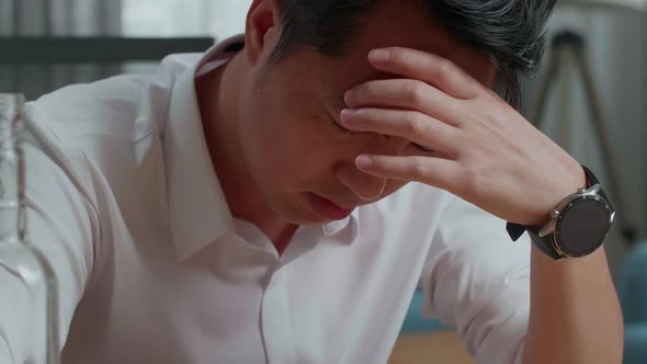 Close Up Of Drunk Asian Man With Vodka Glass Holding The Temples While Sitting On The Chair At Home