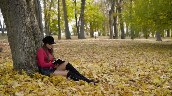 Girl in Stylish Clothes Resting in Park and Writing Down Thoughts in Notebook