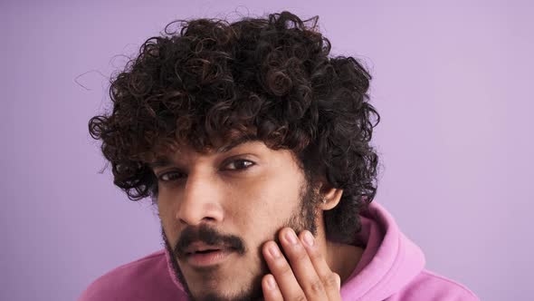 Confident curly-haired Indian man correcting his appearance at the camera
