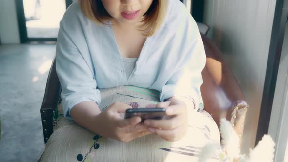 Asian woman using smartphone for talking, reading and texting while sitting on table in cafe.