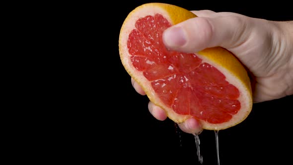 Squeezing out a red juicy grapefruit with a white hand in front of a black background.