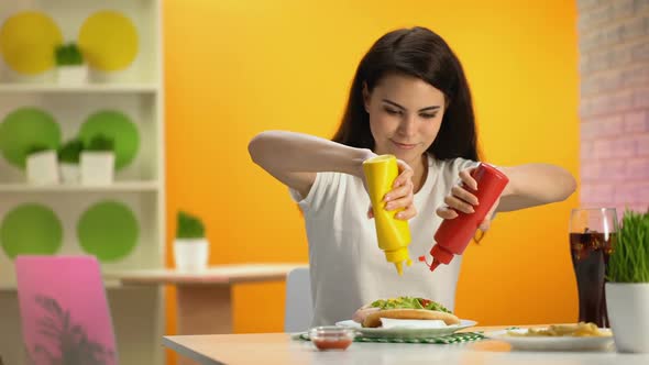 Young Lady Pouring Ketchup and Mustard on Hot-Dog and Smiling on Camera, Canteen