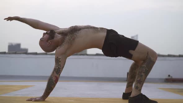 Male Performs Back Bend Yoga Exercise With Both Feet And One Hand On The Ground