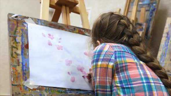 Young Cute Female Artist Is in an Art Studio, Sitting Behind an Easel and Painting on Canvas