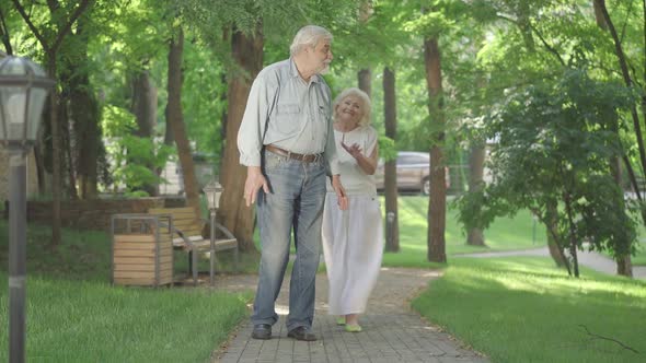 Happy Date of Positive Senior Caucasian Couple in Sunny Summer Park. Smiling Old Man Waiting for