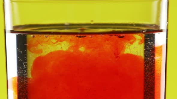 Close Up Footage of Red Ink Dripping Into Clear Water on Yellow Background and Filling It in