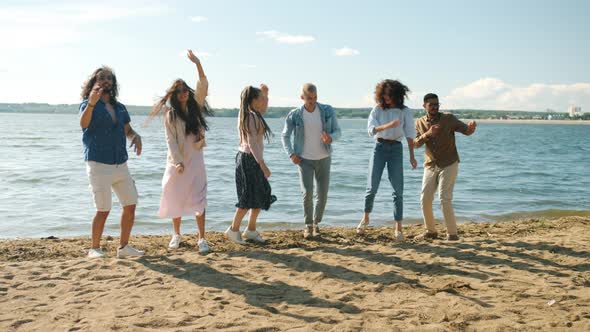 Slow Motion Portrait of Joyful Millennials Dancing on Beach Then Jumping Raising Arms Laughing