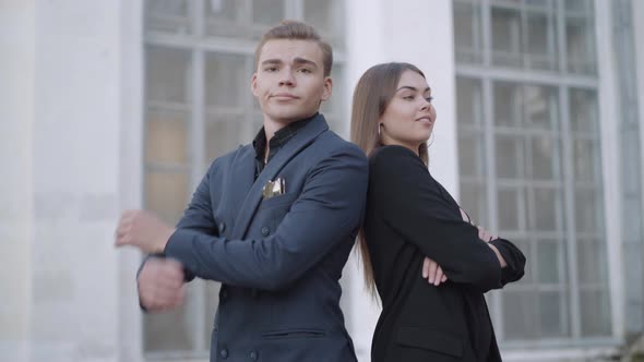 Confident Young Couple Crossing Hands Looking at Camera Standing Back To Back in City