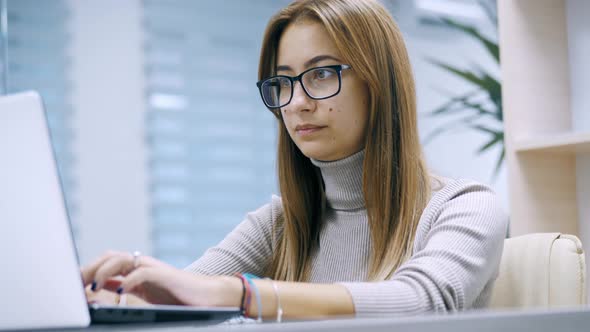 Cute Woman Working at a Laptop with Glasses Typing Text in the Office Employee at Work on the