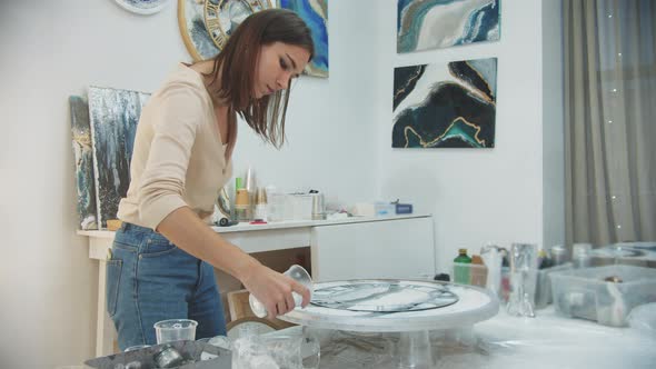 Young Woman Finishes the Epoxy Resin Painting in a Form of Watch and Pouring Clear Pieces Around the