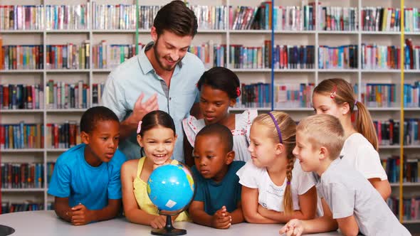 School kids and teacher looking at globe in library