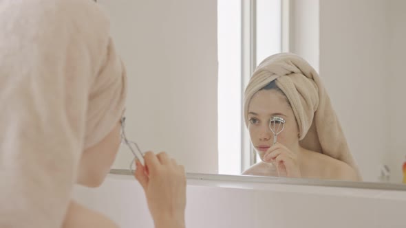 Teenage girl using an eyelash curler in front of the bathroom mirror