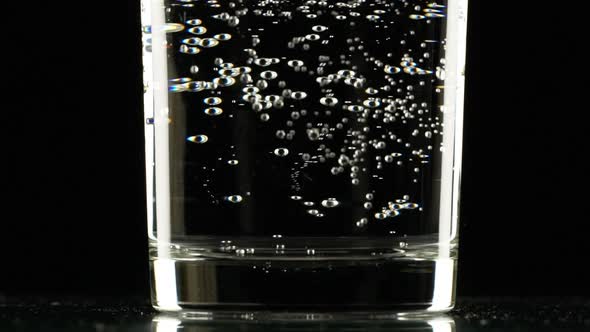 Close Up Footage of Bottom of Glass with Clear Sparkling Water Standing on Black Background in