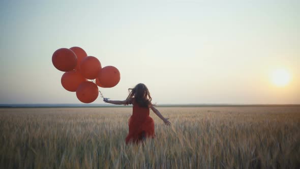 Happy Young Girl with Balloons Running in the Wheat Field at Sunset.  Video.